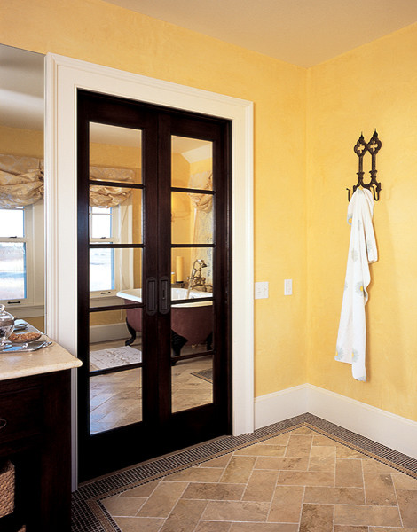 На фото: главная ванная комната среднего размера в классическом стиле с фасадами островного типа, темными деревянными фасадами, ванной на ножках, бежевой плиткой, каменной плиткой, желтыми стенами, полом из известняка и столешницей из известняка с