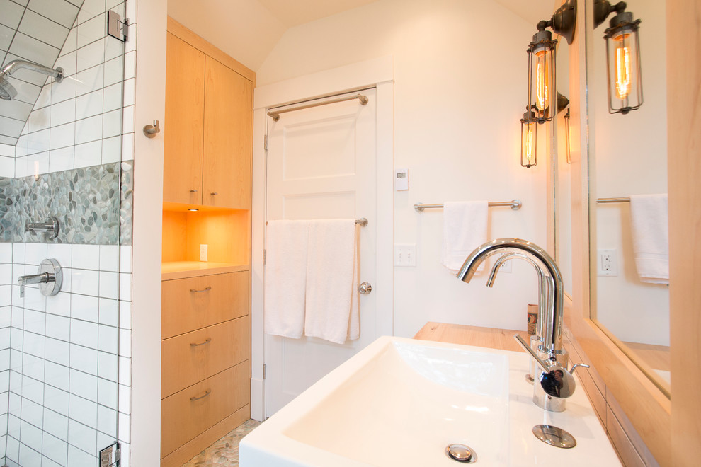Mid-sized elegant 3/4 white tile and ceramic tile pebble tile floor alcove shower photo in Minneapolis with flat-panel cabinets, light wood cabinets, a vessel sink, wood countertops and white walls