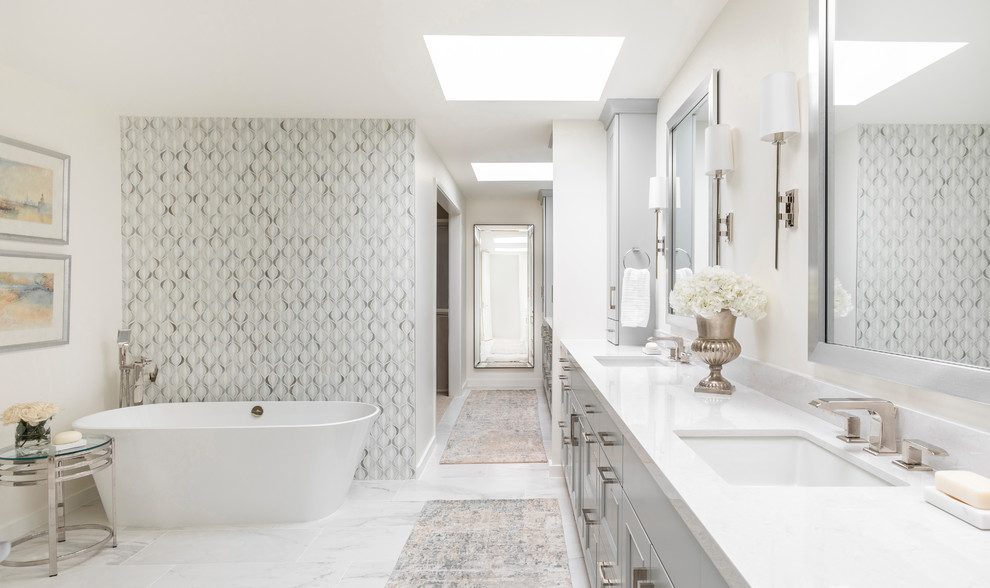 This is an example of a traditional bathroom in Houston with recessed-panel cabinets, grey cabinets, a freestanding bath, grey tiles, white tiles, white walls, a submerged sink, white floors and white worktops.