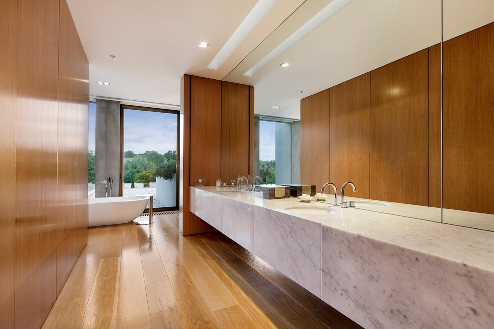 Exemple d'une salle de bain principale moderne en bois brun avec un lavabo encastré, un placard à porte plane, un plan de toilette en marbre, une baignoire indépendante, un mur marron et un sol en bois brun.