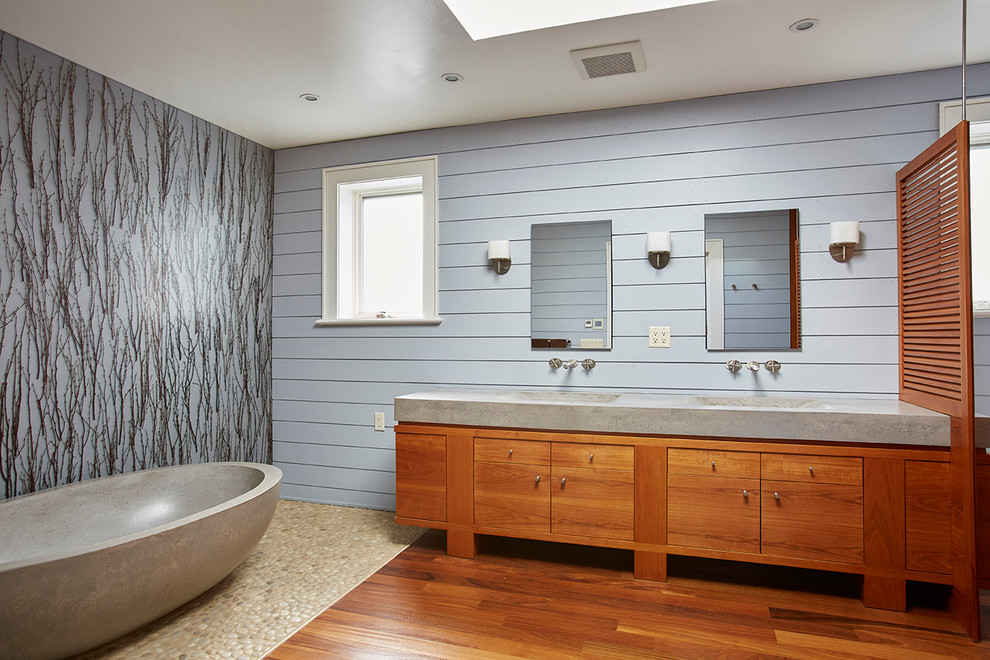 Modern inredning av ett en-suite badrum, med släta luckor, skåp i mellenmörkt trä, ett fristående badkar, blå väggar, klinkergolv i småsten, ett integrerad handfat och bänkskiva i betong