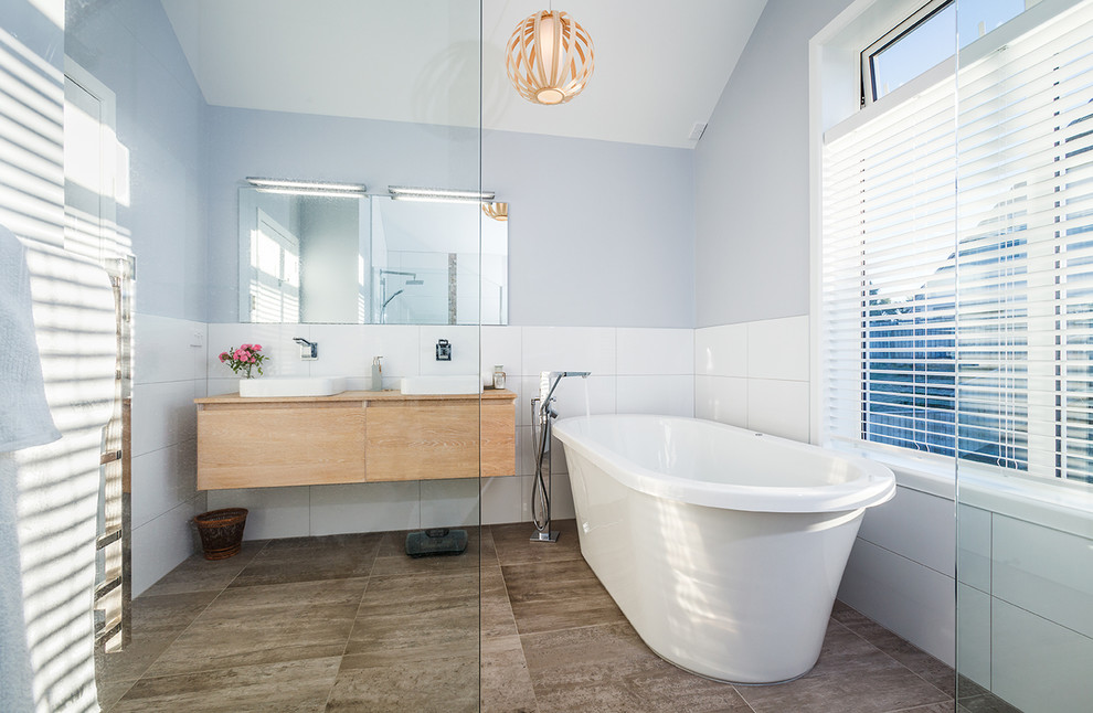 На фото: ванная комната в современном стиле с плоскими фасадами, светлыми деревянными фасадами, отдельно стоящей ванной, коричневой плиткой, белой плиткой, синими стенами, накладной раковиной и открытым душем с
