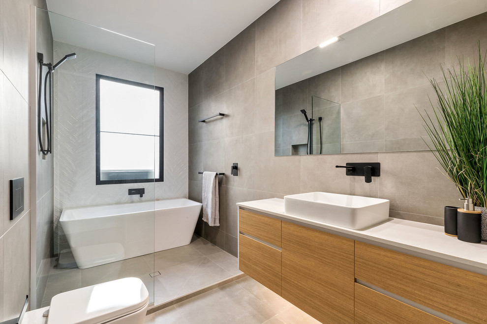 Inredning av ett modernt vit vitt badrum, med släta luckor, skåp i mellenmörkt trä, ett fristående badkar, våtrum, grå kakel, ett fristående handfat, grått golv och med dusch som är öppen