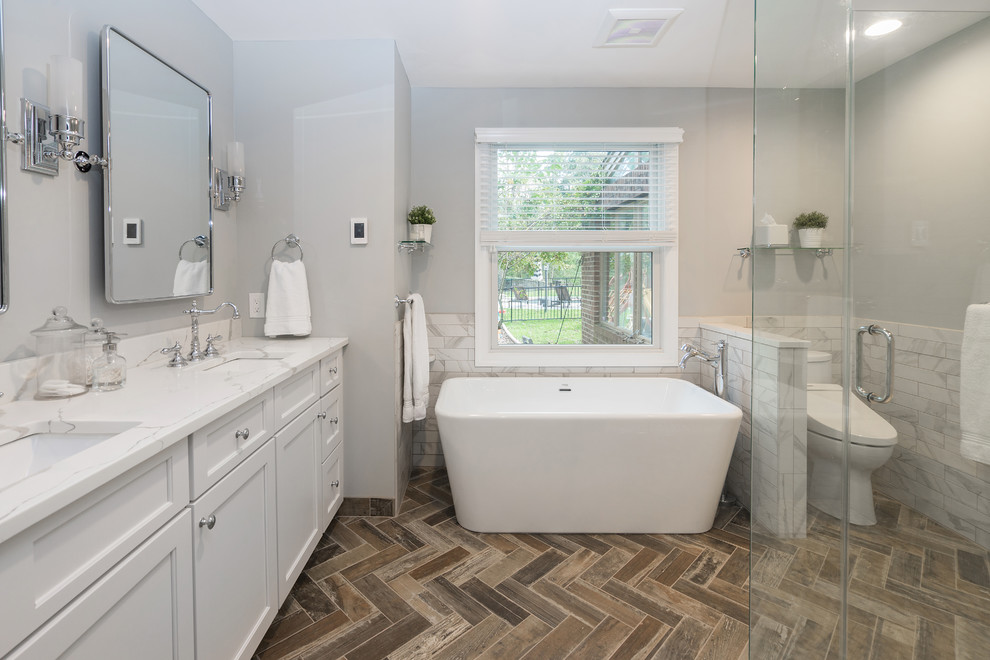 Bathroom - large transitional master white tile and porcelain tile porcelain tile and brown floor bathroom idea in Philadelphia with shaker cabinets, white cabinets, a two-piece toilet, gray walls, an undermount sink, quartz countertops, a hinged shower door and white countertops