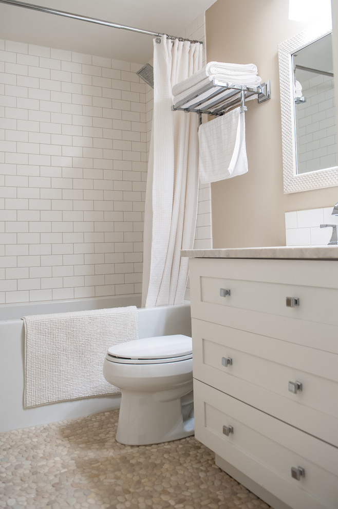 This is an example of a small farmhouse bathroom in Calgary with shaker cabinets, white cabinets, an alcove bath, a shower/bath combination, white tiles, cement tiles, beige walls, pebble tile flooring, a submerged sink, a two-piece toilet and beige floors.