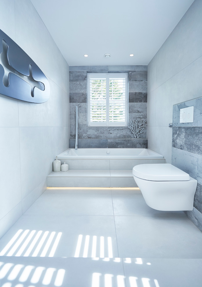 This is an example of a large contemporary ensuite bathroom in Devon with grey cabinets, a built-in bath, a walk-in shower, a wall mounted toilet, grey tiles, porcelain tiles, beige walls, a wall-mounted sink and porcelain flooring.