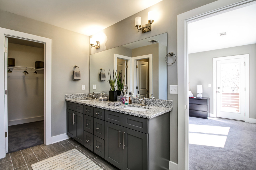 Cette image montre une salle de bain principale traditionnelle de taille moyenne avec un placard à porte shaker, des portes de placard grises, un mur gris, un sol en carrelage de porcelaine, un lavabo encastré, un plan de toilette en granite et un sol marron.