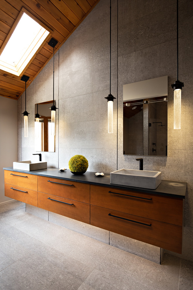 Inspiration for a large contemporary master gray tile gray floor and concrete floor double shower remodel in Other with flat-panel cabinets, medium tone wood cabinets, a one-piece toilet, gray walls, a vessel sink, a hinged shower door, black countertops and concrete countertops