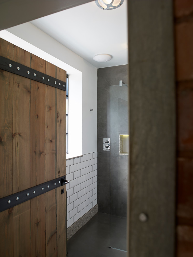 Diseño de cuarto de baño urbano con ducha abierta, sanitario de dos piezas, paredes grises, suelo de cemento, aseo y ducha y lavabo suspendido