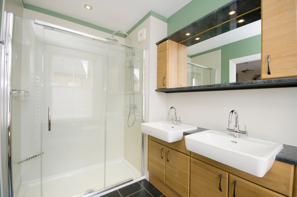 Modelo de cuarto de baño moderno con lavabo integrado, armarios con paneles lisos, puertas de armario de madera oscura, encimera de laminado, ducha empotrada, sanitario de una pieza, paredes verdes y suelo de linóleo