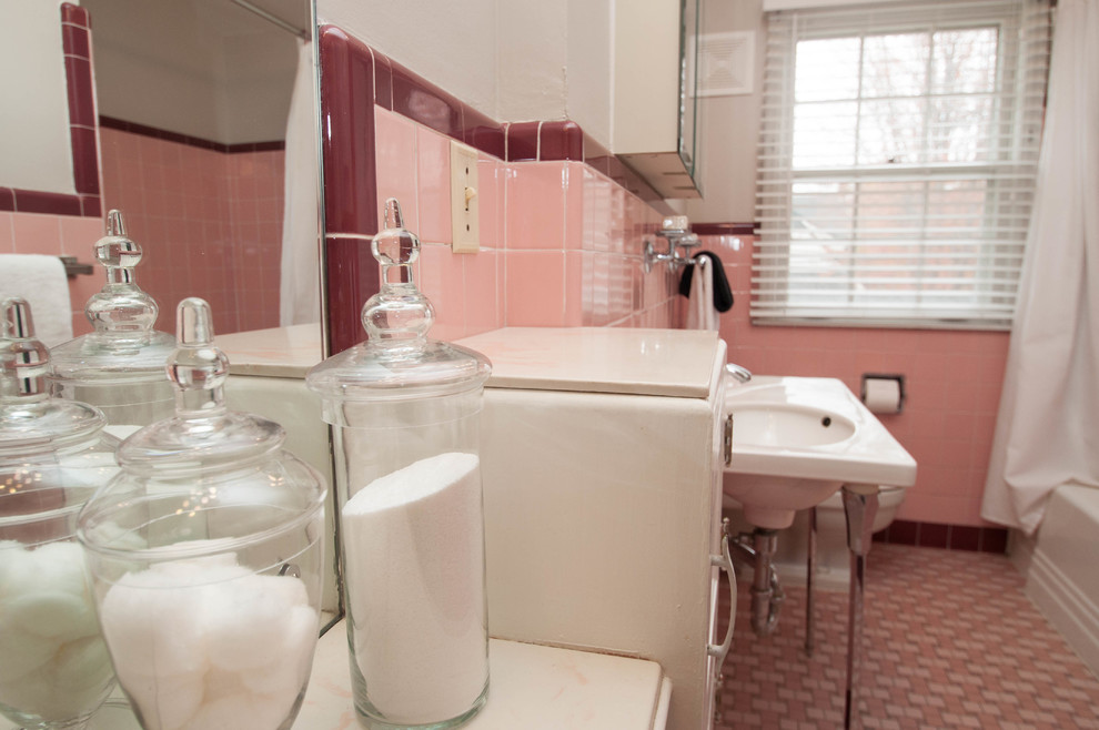 Foto på ett mellanstort vintage vit badrum för barn, med luckor med infälld panel, vita skåp, ett platsbyggt badkar, en dusch/badkar-kombination, en toalettstol med hel cisternkåpa, rosa kakel, keramikplattor, vita väggar, klinkergolv i keramik, ett piedestal handfat, träbänkskiva, rosa golv och dusch med duschdraperi
