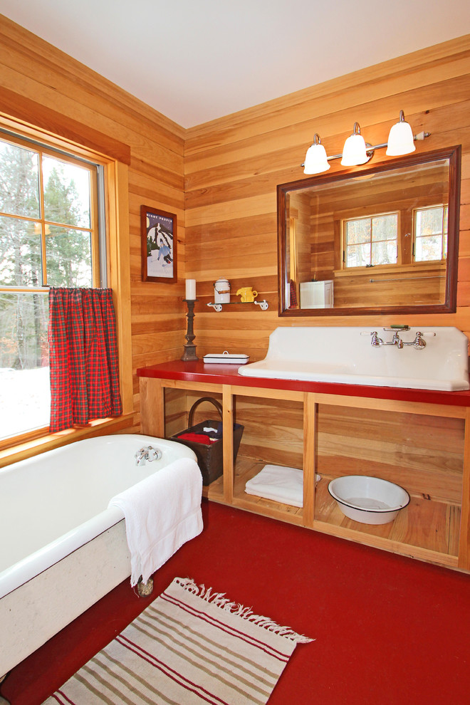 Cette image montre une salle de bain principale chalet en bois clair de taille moyenne avec une grande vasque, un placard sans porte, une baignoire sur pieds, un sol en terrazzo, un plan de toilette en surface solide et un sol rouge.