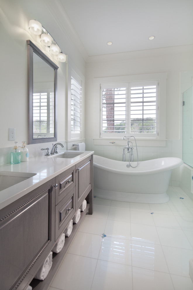 Diseño de cuarto de baño costero con lavabo bajoencimera, armarios con paneles con relieve, puertas de armario grises, bañera exenta, baldosas y/o azulejos blancos y paredes blancas