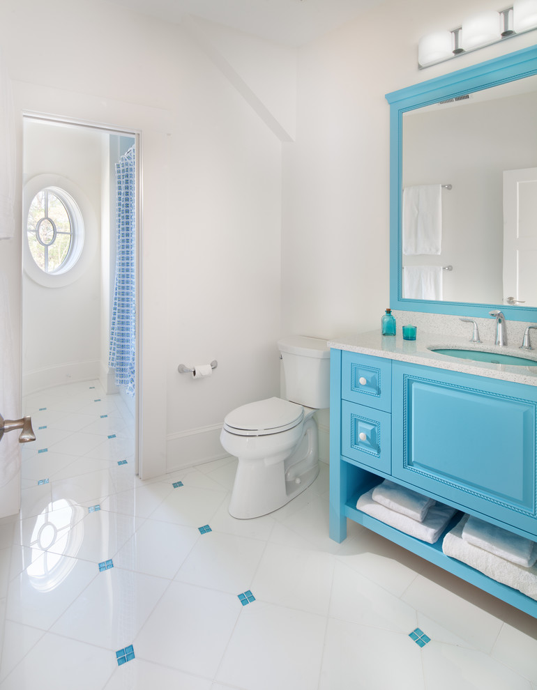 Diseño de cuarto de baño costero con lavabo bajoencimera, puertas de armario azules, sanitario de dos piezas, paredes blancas y armarios con paneles con relieve