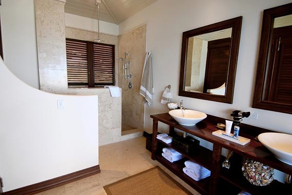 Idéer för att renovera ett mellanstort tropiskt brun brunt en-suite badrum, med öppna hyllor, skåp i mörkt trä, en dusch i en alkov, beige kakel, stenhäll, vita väggar, travertin golv, ett fristående handfat, träbänkskiva, brunt golv och med dusch som är öppen