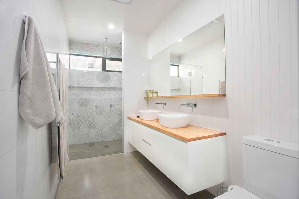 Bild på ett mellanstort funkis en-suite badrum, med släta luckor, vita skåp, en hörndusch, en toalettstol med separat cisternkåpa, vit kakel, vita väggar, betonggolv, ett fristående handfat, träbänkskiva, grått golv och dusch med gångjärnsdörr