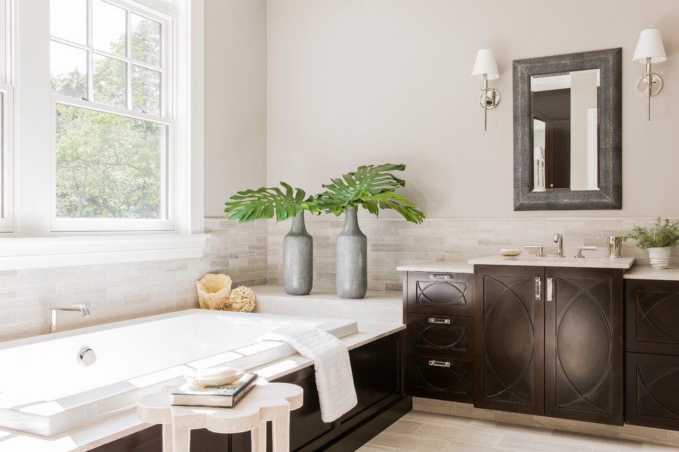 Klassisk inredning av ett stort en-suite badrum, med skåp i mörkt trä, ett platsbyggt badkar, beige kakel, stenkakel, beige väggar, klinkergolv i porslin, ett undermonterad handfat och beiget golv