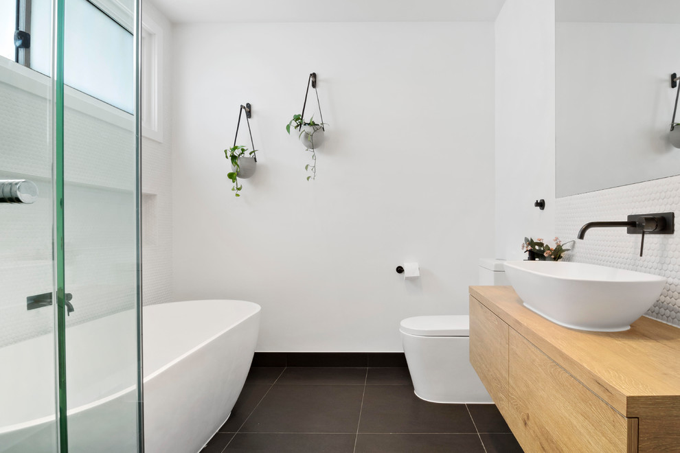 Modern inredning av ett brun brunt en-suite badrum, med svarta skåp, ett fristående badkar, vit kakel, vita väggar, ett fristående handfat, träbänkskiva, svart golv och dusch med gångjärnsdörr