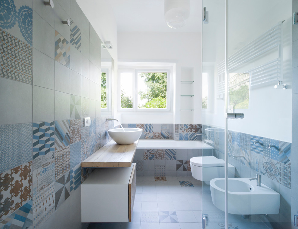 Modern inredning av ett en-suite badrum, med ett fristående handfat, släta luckor, skåp i ljust trä, ett platsbyggt badkar, en bidé, keramikplattor, klinkergolv i keramik, flerfärgade väggar och flerfärgad kakel