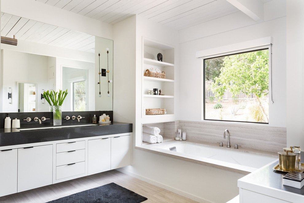 Diseño de cuarto de baño actual con armarios con paneles lisos, bañera encastrada sin remate, paredes blancas, lavabo bajoencimera y espejo con luz