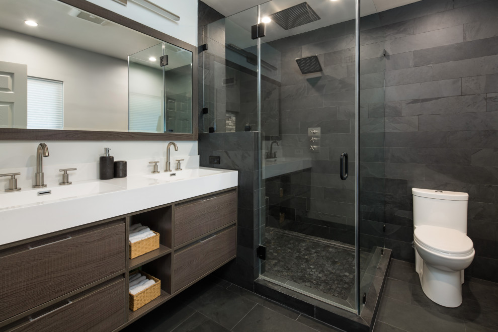 Пример оригинального дизайна: главная ванная комната среднего размера в стиле неоклассика (современная классика) с плоскими фасадами, темными деревянными фасадами, угловым душем, унитазом-моноблоком, черной плиткой, плиткой из сланца, серыми стенами, полом из сланца, монолитной раковиной, столешницей из искусственного камня, черным полом, душем с распашными дверями, белой столешницей, сиденьем для душа, тумбой под две раковины и подвесной тумбой