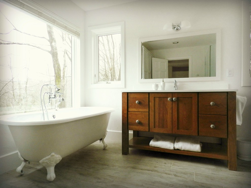 This is an example of a large country ensuite bathroom in New York with shaker cabinets, medium wood cabinets, a claw-foot bath, a built-in shower, a two-piece toilet, white tiles, white walls, vinyl flooring, an integrated sink, solid surface worktops, grey floors and a hinged door.