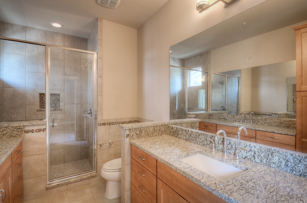 Photo of a medium sized traditional ensuite bathroom in Austin with a submerged sink, recessed-panel cabinets, medium wood cabinets, granite worktops, a shower/bath combination, a two-piece toilet, beige tiles, porcelain tiles, beige walls and porcelain flooring.
