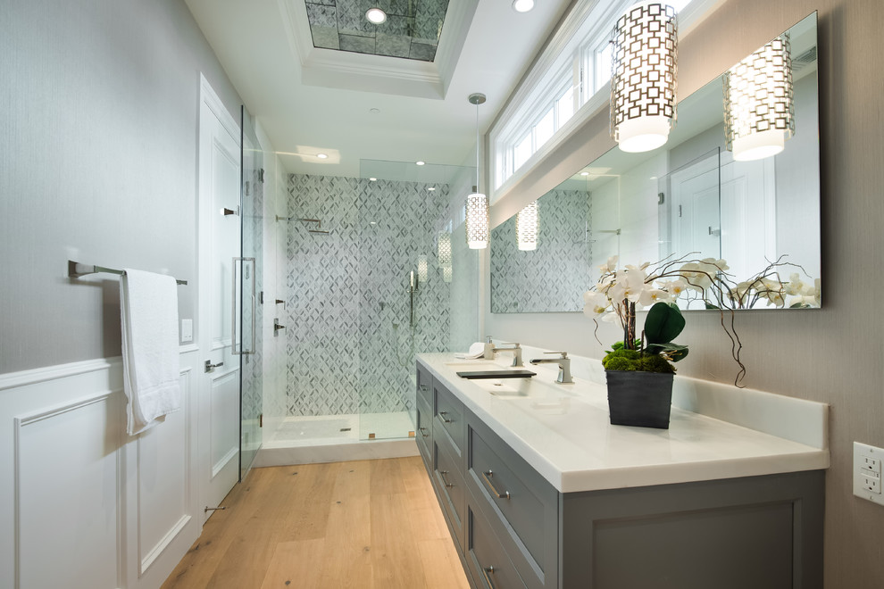Bild på ett stort vintage badrum med dusch, med luckor med infälld panel, grå skåp, en dusch i en alkov, grå kakel, mosaik, grå väggar, ljust trägolv, ett undermonterad handfat och marmorbänkskiva