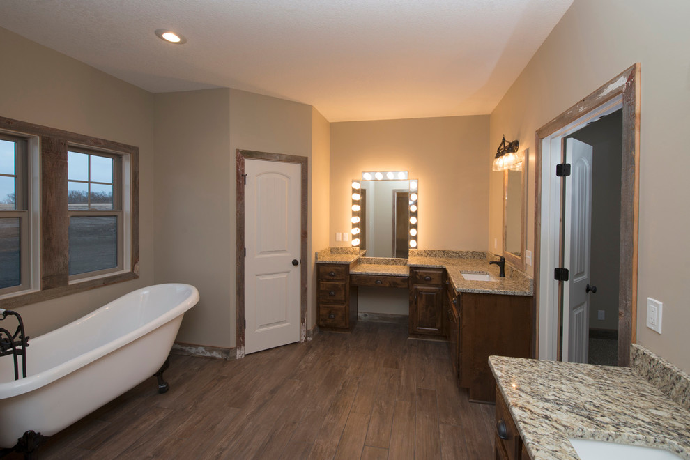Klassisk inredning av ett stort en-suite badrum, med luckor med upphöjd panel, skåp i mörkt trä, ett badkar med tassar, beige väggar, mellanmörkt trägolv, ett undermonterad handfat och granitbänkskiva