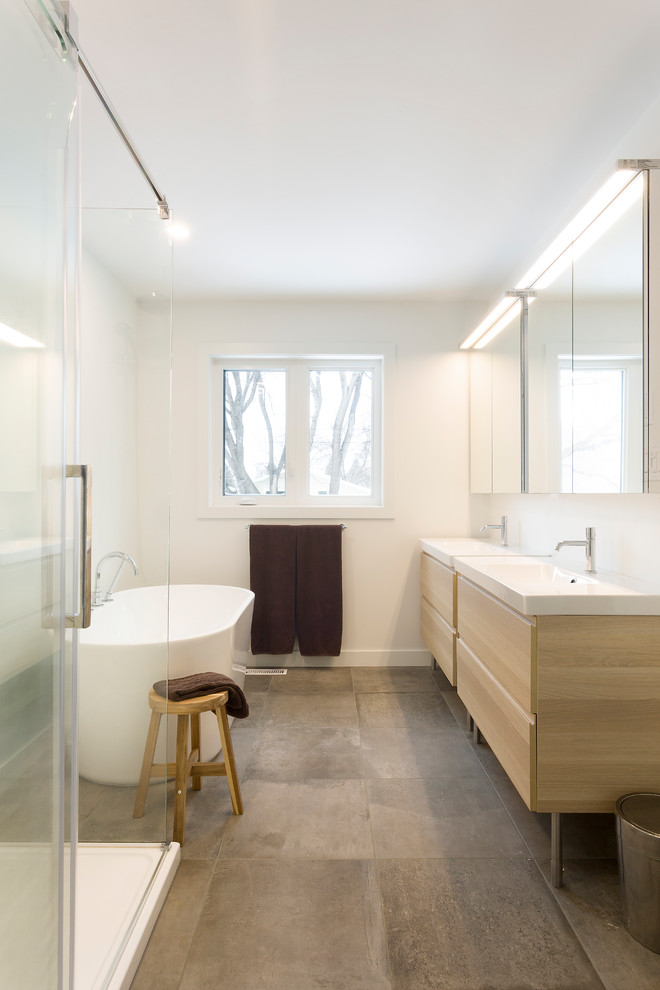 Idées déco pour une grande salle de bain principale scandinave en bois clair avec un placard à porte plane, une baignoire indépendante, une douche d'angle, un sol en carrelage de porcelaine, un lavabo intégré, un plan de toilette en surface solide, un sol gris et une cabine de douche à porte battante.