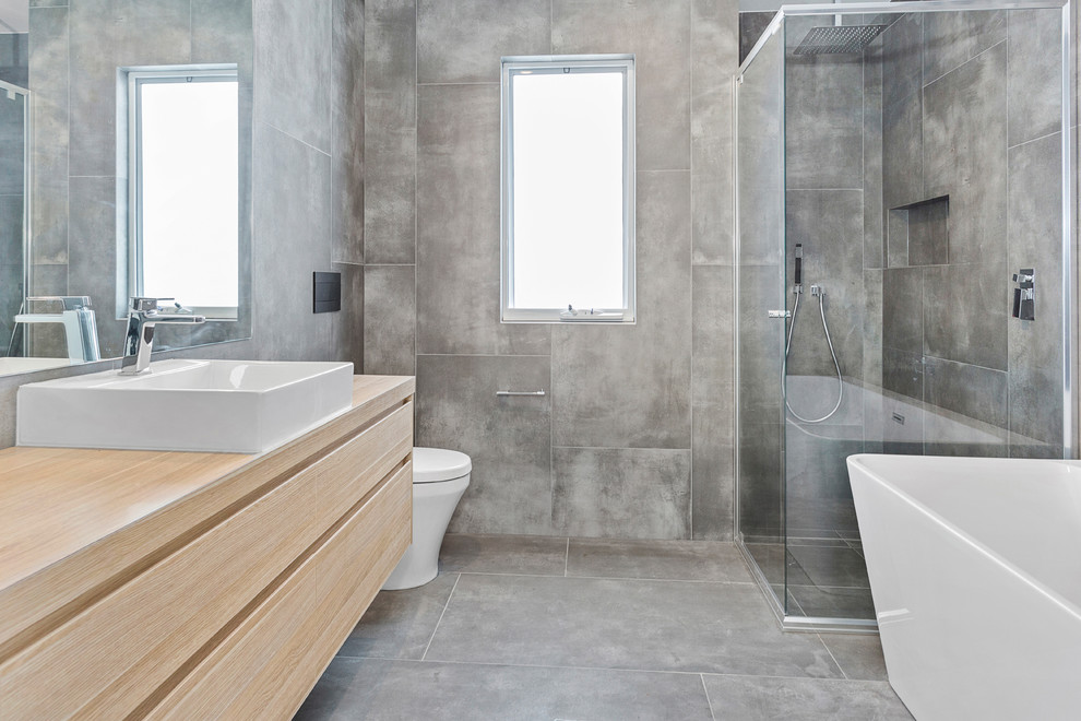 Exempel på ett modernt badrum, med släta luckor, skåp i ljust trä, ett fristående badkar, en hörndusch, grå kakel, ett fristående handfat, träbänkskiva, grått golv och dusch med gångjärnsdörr