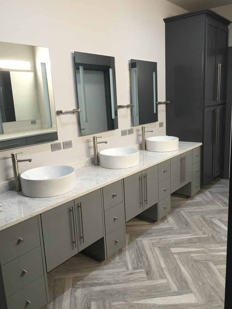 Cette photo montre une grande salle de bain principale chic avec un placard à porte plane, des portes de placard grises, un mur blanc, un sol en bois brun, une vasque, un plan de toilette en marbre, un sol gris et un plan de toilette blanc.