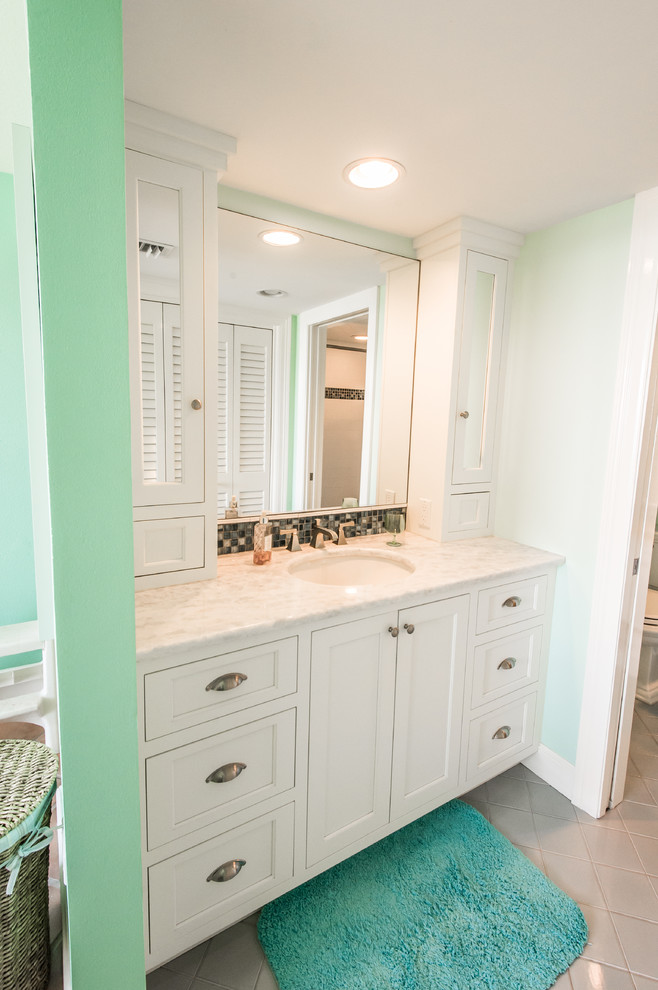 Example of a mid-sized beach style 3/4 beige tile, black and white tile, brown tile and mosaic tile bathroom design in Miami with recessed-panel cabinets, white cabinets, a two-piece toilet, green walls, an undermount sink and granite countertops