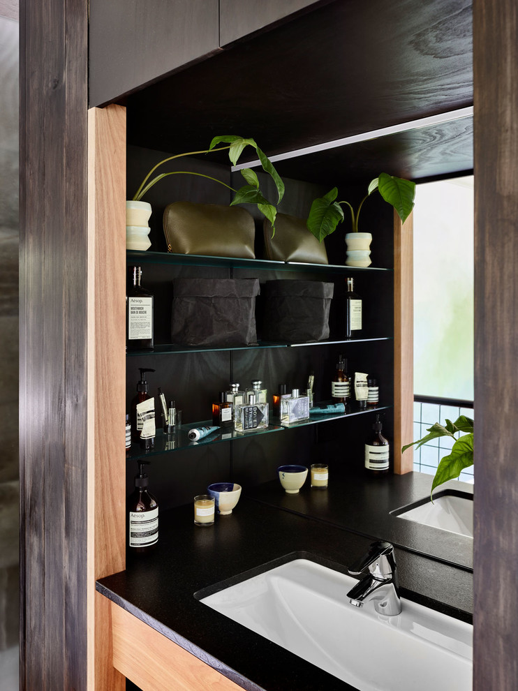 Inspiration for a small modern ensuite bathroom in Brisbane with flat-panel cabinets, light wood cabinets, black walls, light hardwood flooring, a submerged sink and granite worktops.