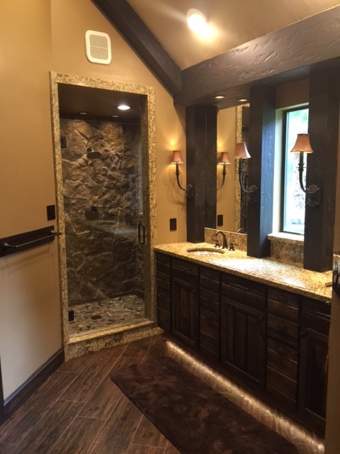 Photo of a medium sized rustic ensuite bathroom in Houston with raised-panel cabinets, dark wood cabinets, a double shower, a one-piece toilet, yellow tiles, stone slabs, yellow walls, porcelain flooring, a submerged sink and granite worktops.