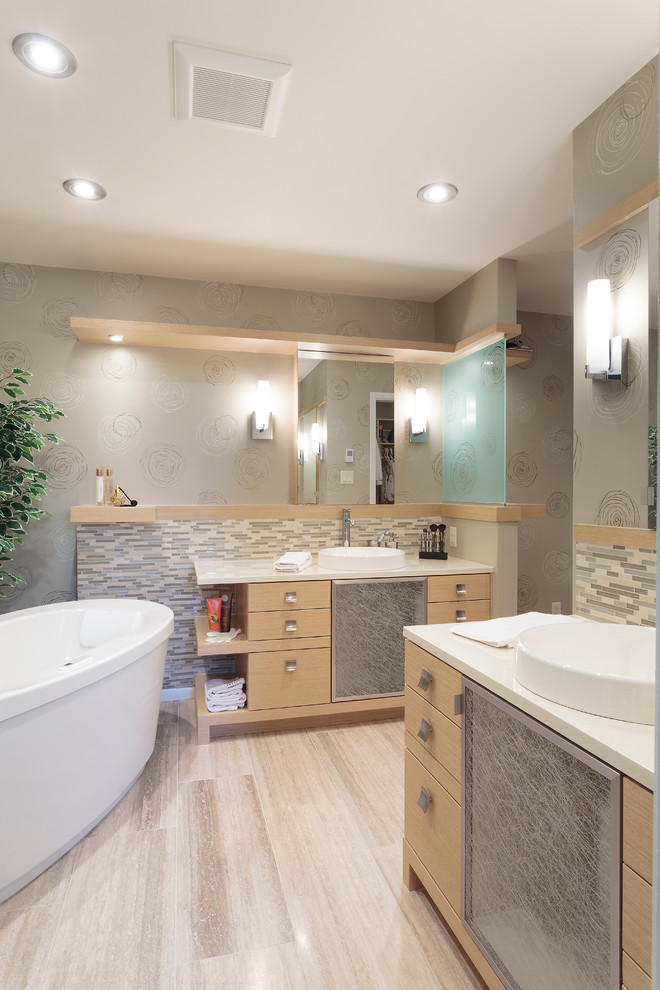 Cette image montre une grande salle de bain principale design en bois clair avec une baignoire indépendante, une vasque, un placard à porte plane, un mur gris et un sol beige.