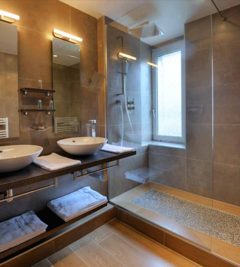 Photo of a large modern shower room bathroom in Other with open cabinets, a corner shower, brown tiles, porcelain tiles, light hardwood flooring, a vessel sink, engineered stone worktops, brown floors, a hinged door and brown worktops.