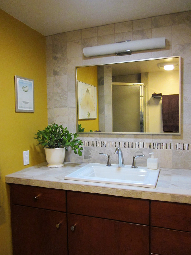 Immagine di una piccola stanza da bagno per bambini tradizionale con ante lisce, ante in legno bruno, piastrelle beige, piastrelle in ceramica, pareti gialle, lavabo da incasso e top piastrellato