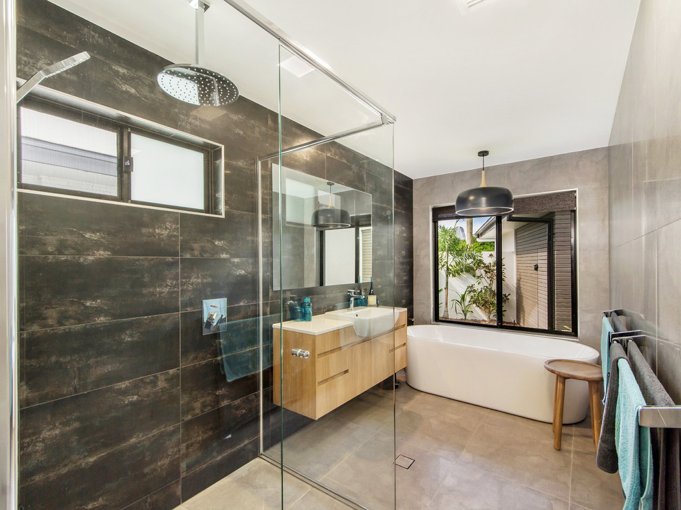 Стильный дизайн: ванная комната в современном стиле с светлыми деревянными фасадами, отдельно стоящей ванной, угловым душем, серой плиткой и настольной раковиной - последний тренд