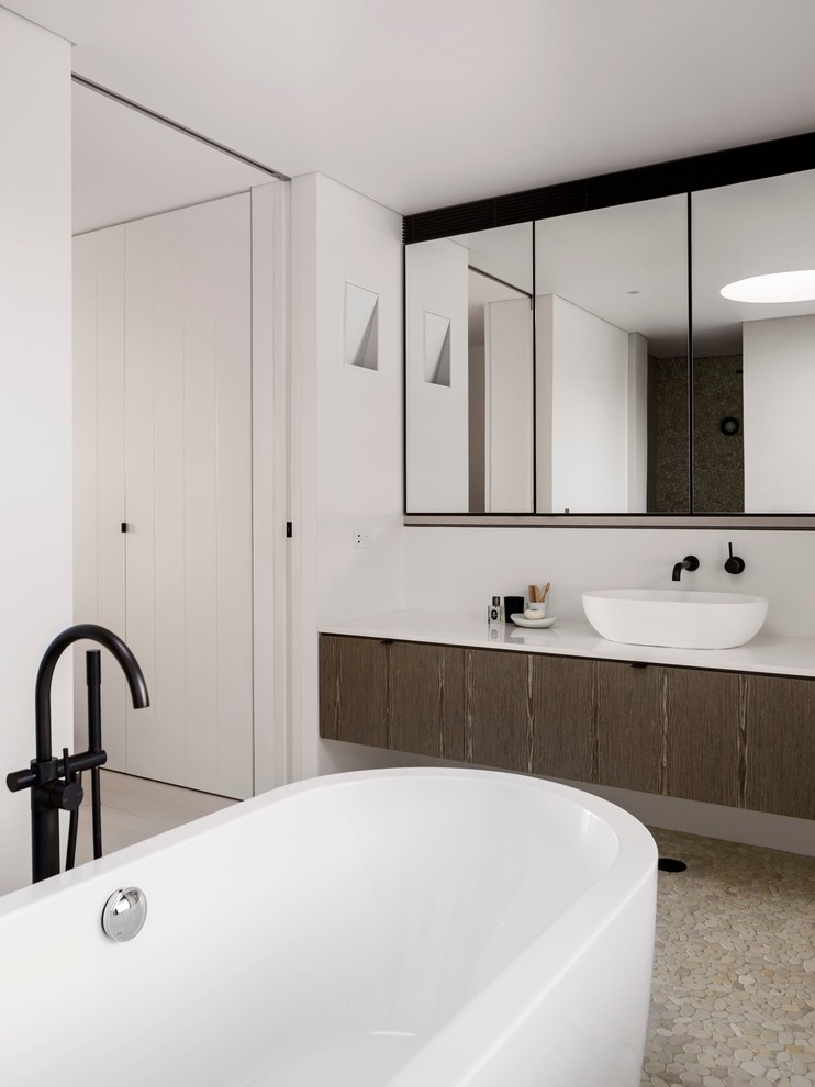 Idée de décoration pour une grande salle de bain design avec des portes de placard blanches, une baignoire indépendante, un carrelage beige, un mur blanc, une vasque et un plan de toilette en marbre.