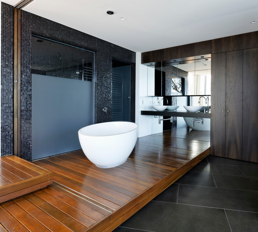 Idées déco pour une grande douche en alcôve principale contemporaine en bois foncé avec une vasque, une baignoire indépendante, un mur noir, un sol en bois brun, un placard à porte plane, un plan de toilette en bois, un carrelage noir et mosaïque.