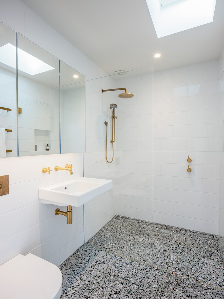 Inredning av ett modernt badrum, med en kantlös dusch, en vägghängd toalettstol, vit kakel, vita väggar, ett väggmonterat handfat, grått golv och med dusch som är öppen
