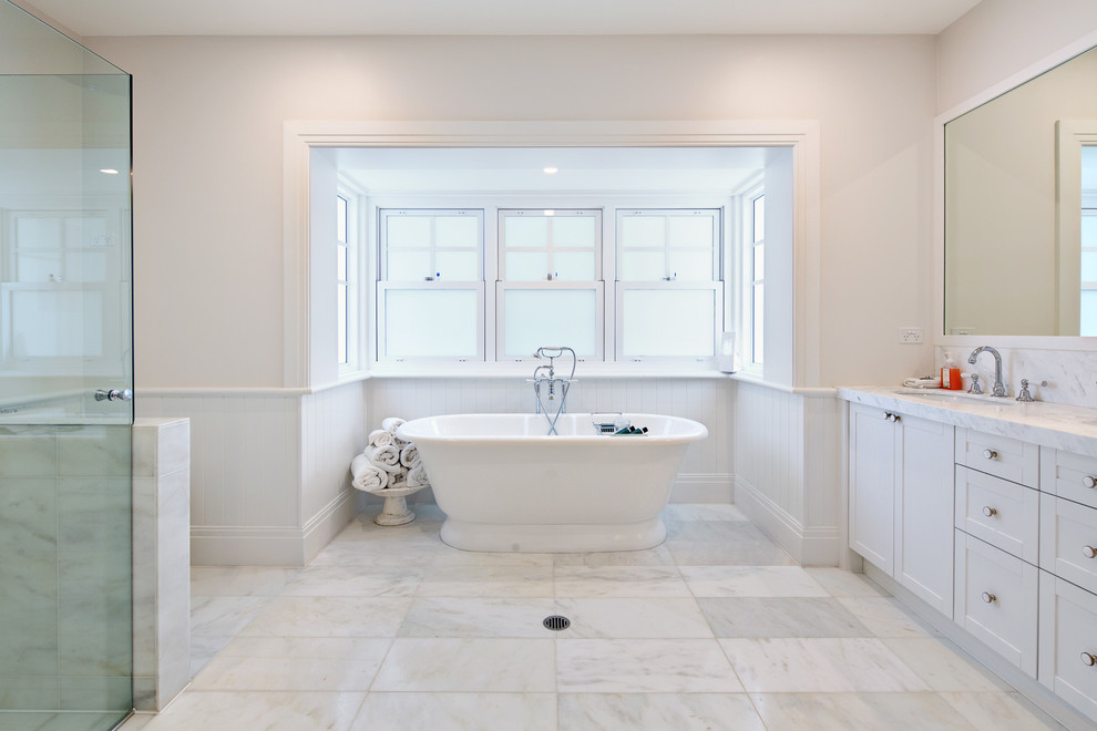 Foto de cuarto de baño principal clásico grande con armarios estilo shaker, puertas de armario blancas, bañera empotrada, ducha doble, baldosas y/o azulejos blancos y encimera de mármol
