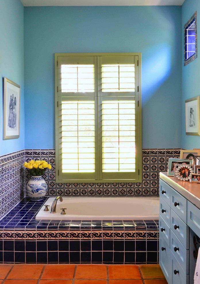 This is an example of a large mediterranean bathroom in Houston with shaker cabinets, blue cabinets, a built-in bath, blue tiles, mosaic tiles, blue walls, terracotta flooring and red floors.
