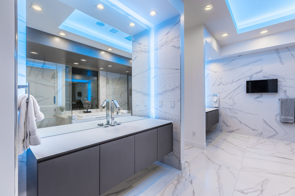 Идея дизайна: большая главная ванная комната в современном стиле с плоскими фасадами, серыми фасадами, накладной ванной, угловым душем, белой плиткой, керамогранитной плиткой, белыми стенами, полом из керамогранита, монолитной раковиной, стеклянной столешницей, белым полом и душем с распашными дверями