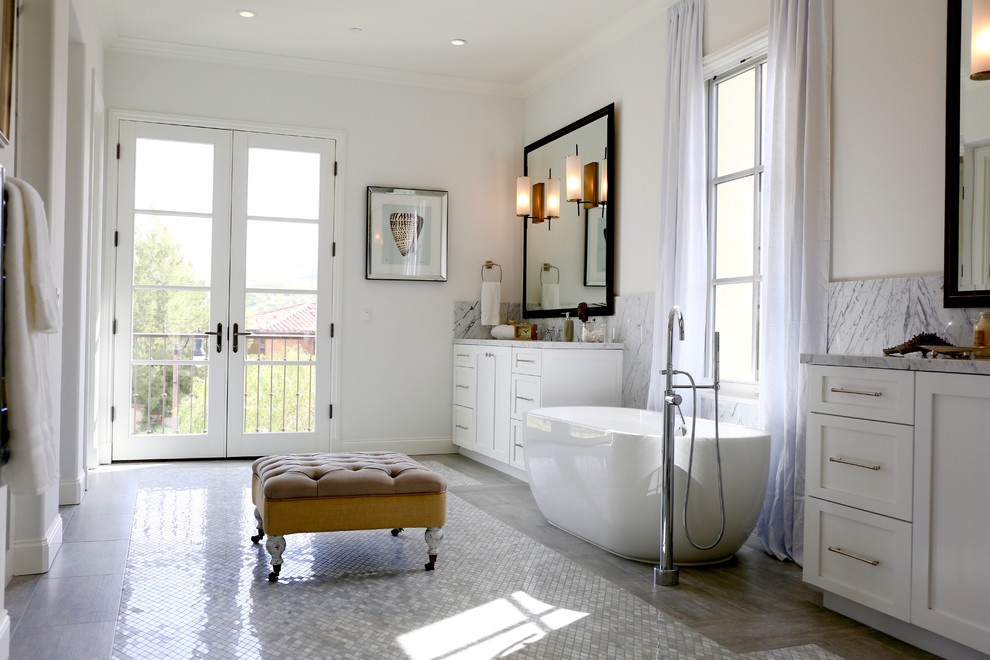На фото: огромная главная ванная комната в классическом стиле с фасадами в стиле шейкер, белыми фасадами, отдельно стоящей ванной, серой плиткой, разноцветной плиткой, белой плиткой, белыми стенами, полом из керамогранита, врезной раковиной и мраморной столешницей с