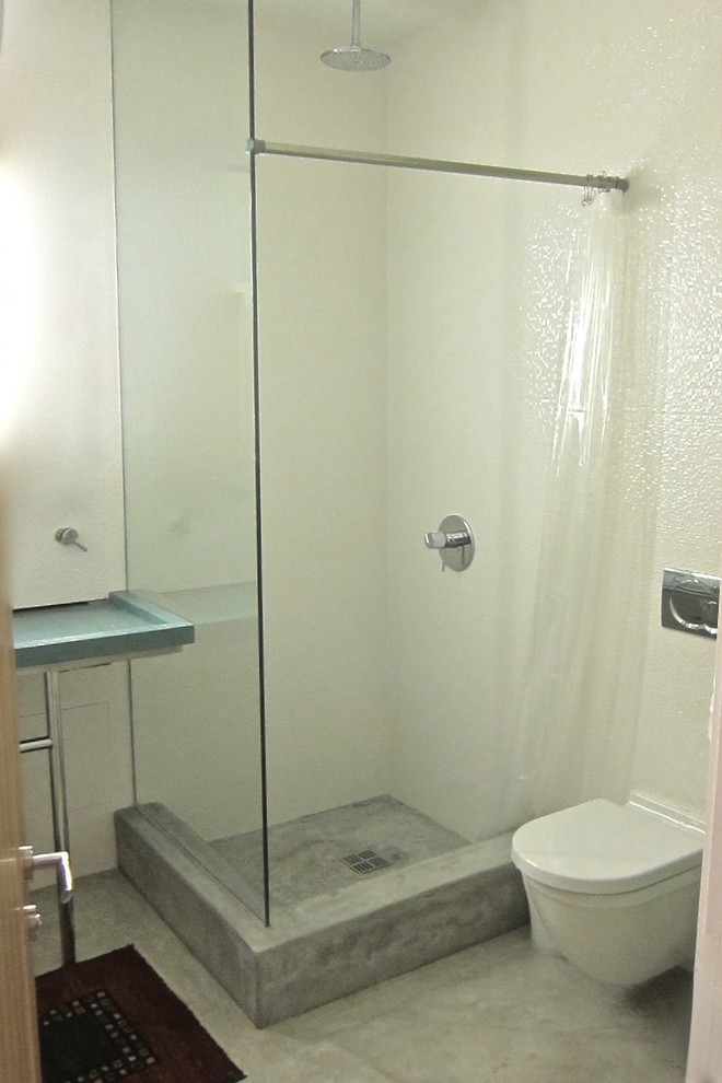 This is an example of a medium sized contemporary shower room bathroom in Los Angeles with an integrated sink, flat-panel cabinets, white cabinets, concrete worktops, a corner shower, a wall mounted toilet, white tiles, porcelain tiles, white walls and concrete flooring.