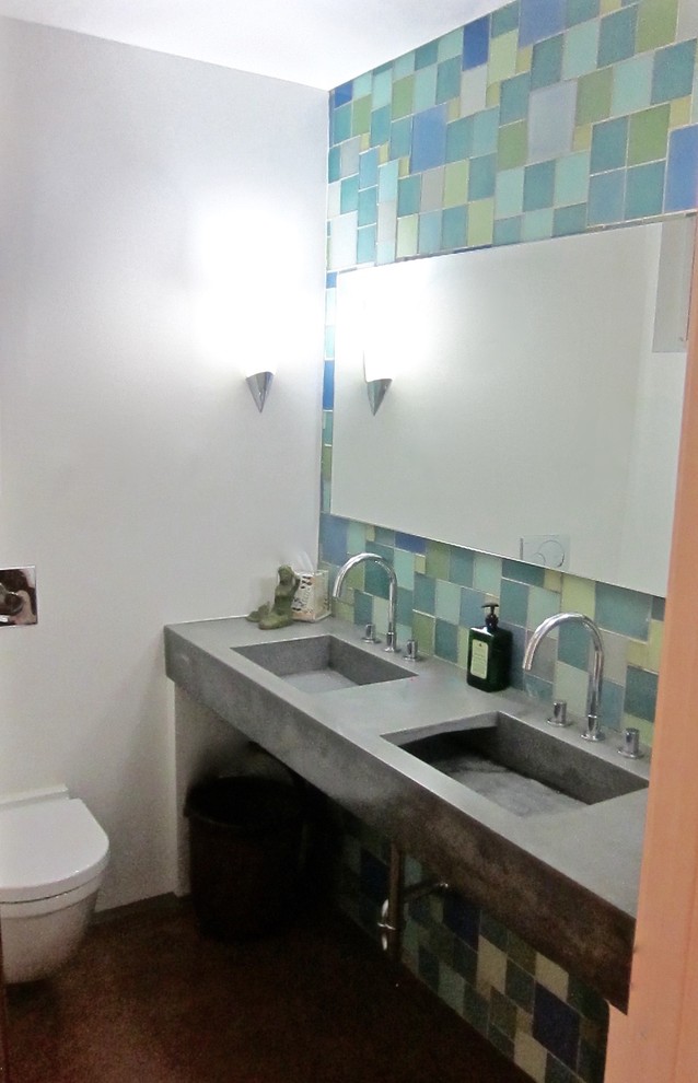 Diseño de cuarto de baño contemporáneo de tamaño medio con lavabo integrado, armarios abiertos, encimera de cemento, sanitario de pared, baldosas y/o azulejos azules, baldosas y/o azulejos de vidrio, paredes blancas, suelo de cemento y aseo y ducha