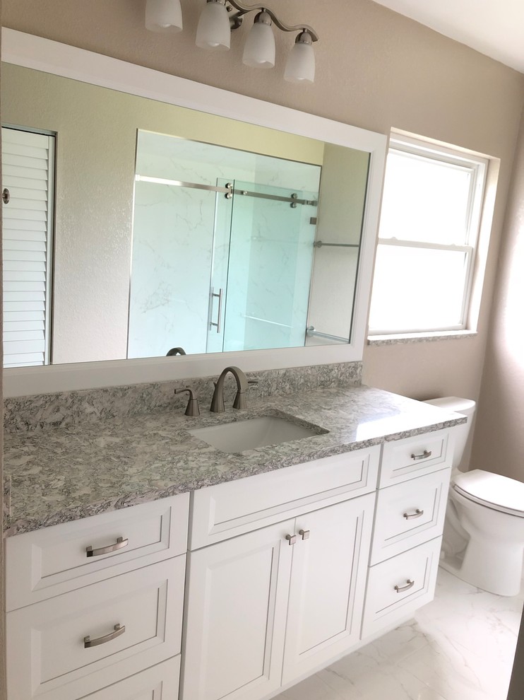 Inspiration for a mid-sized transitional 3/4 white tile and porcelain tile porcelain tile and white floor bathroom remodel in Tampa with recessed-panel cabinets, white cabinets, a one-piece toilet, beige walls, an undermount sink, quartz countertops and gray countertops