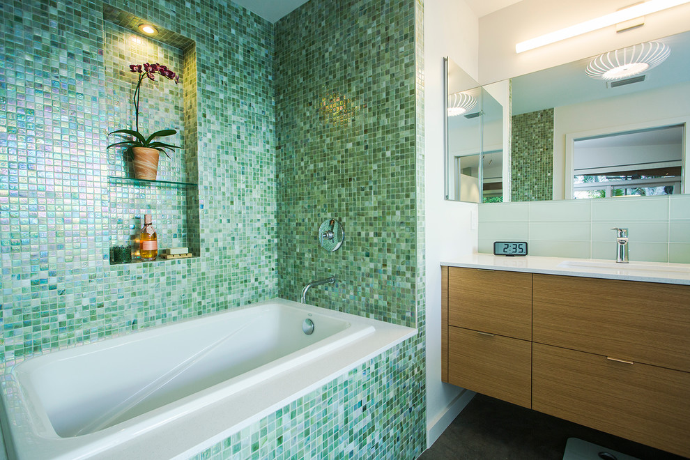 Modelo de cuarto de baño principal retro con armarios con paneles lisos, puertas de armario de madera clara, bañera empotrada, baldosas y/o azulejos verdes, baldosas y/o azulejos en mosaico, paredes blancas y suelo de cemento